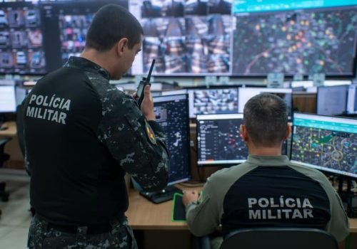 Policiais militares de Goiás em central de monitoramento com telões de câmeras e mapas do programa IA Contra o Crime